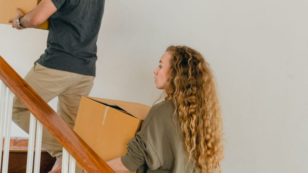 People carrying cardboard boxes up an indoor staircase during a move